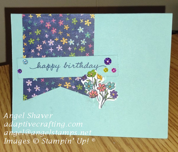 Birthday card with flag of patterned paper will small bright flowers with dies of bouquet of flowers adhered to sentiment strip.  Bright glossy dots are on happy birthday sentiment strip.