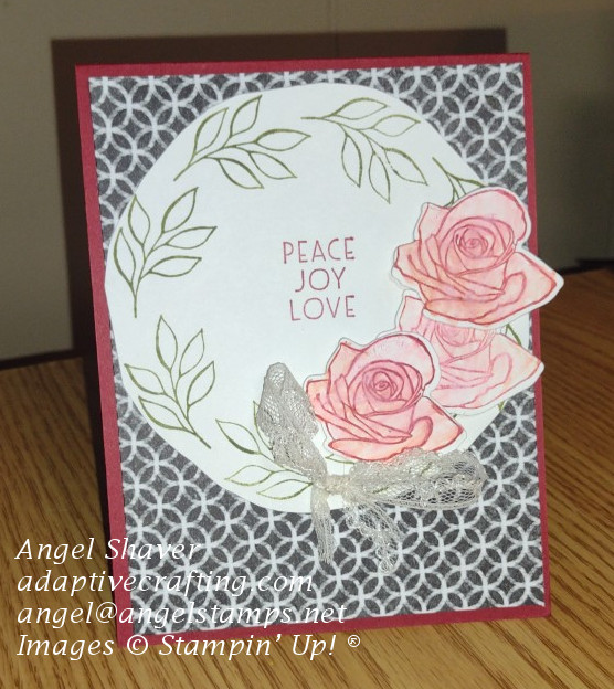 Cherry red Christmas card with black & white patterned paper front with a circle wreath with green leaves  and red roses with a vintage lace bow.  Says "peace, joy, love" in the center of the wreath.