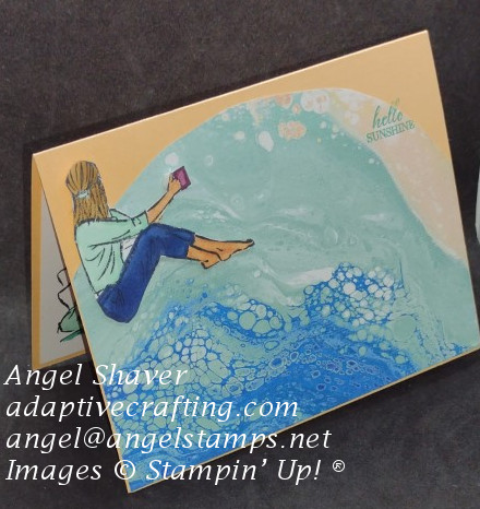 Card made to represent the beach with patterned paper representing ocean waves.  A girl sits with cup in hand looking out at the beach.  