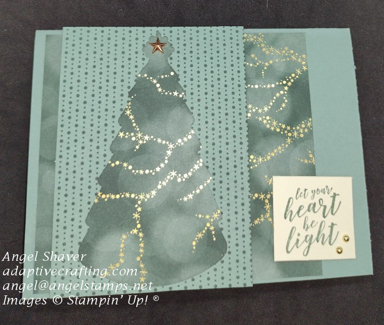 Green Christmas card with die cut Christmas tree on top layer with bottom layer of streaks of gold stars on a dark green background showing through the die cut image.  Sentiment says "Let your heart be light."