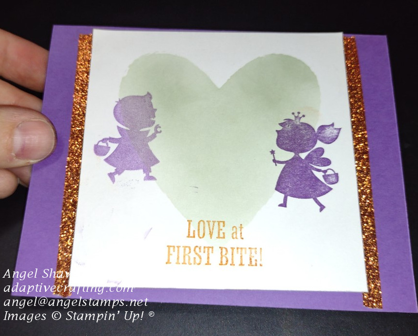 Purple card with a green ink blended heart with two costumed characters walking toward each other.  The sentiment says, "Love at First Bite!"