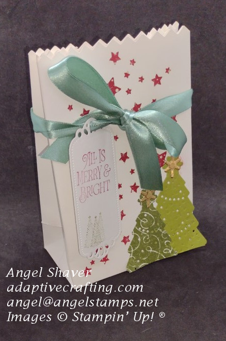 White gift bag with cut out stars.  Red paper behind the stars.  Die cut green trees with gold stars.  Bag tied with green ribbon.  Gift tag hanging from ribbon with stamped green trees and red sentiment, "All is merry and bright."