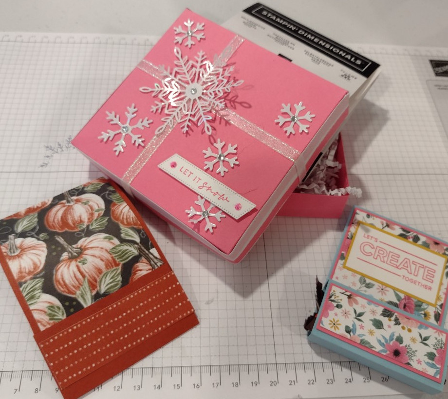 Pink box with snowflake decorations open to reveal Stampin' Dimensionals.  Two treat packages: One with pumpkin patterned paper and one with floral patterned paper that says "Let's Create Together."