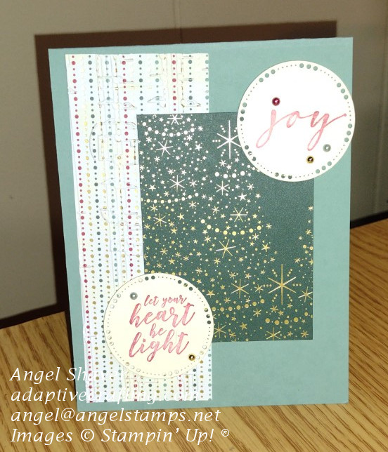 Green Christmas card with strip of patterned paper embossed with music pattern on left side of card.  Green rectangle of patterned paper on top of that with gold Christmas trees and two small sentiment circles with pearls.  One says "joy" and the other says "let your heart be light."