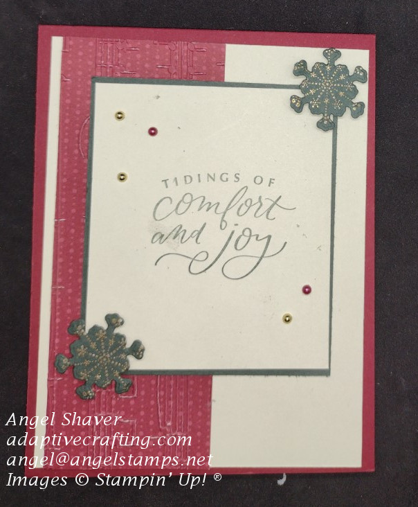 Red Christmas card with strip of patterned paper embossed with music pattern on left side of card.  Framed sentiment rectangle in center of card that says, "tidings of comfort and joy"  Two green snowflakes heat embossed with gold on top right and bottom left of sentiment rectangle.
