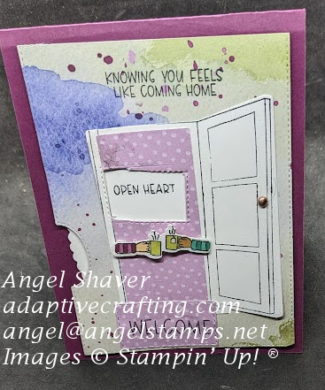 Purple card with background paper with blobs and splatters of color.  Diecut of open door with two arms with cups stretching across door.  Welcome mat in front of door.  Rotating wheel of sentiments says "Open heart." Sentiment at top of card says, "Knowing you feels like coming home."