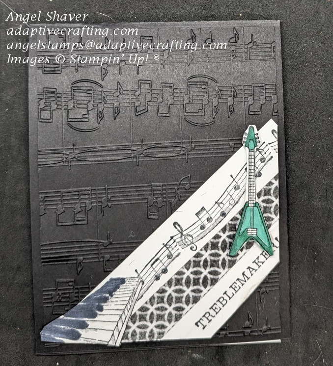 Black card with music embossed background paper.  Three diagonal strips of paper at the bottom of the card: 1 stamped with music score, 1 black & white patterned paper, 1 with sentiment "treblemaker".  Keyboard and guitar are adhered to tope.