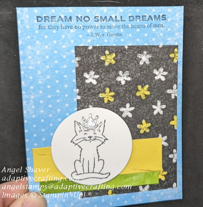 Card with turquoise background with polka dots.  Card is layred with black and white printed paper with flowers, some are colored yellow and two strips of paper: 1 yellow, 1 green.  The top layer is a circle with a stamp of a white cat wearing a silver crown. 
Sentiment says, "Dream no small dreams for they have no power to move the hearts of men.--J.W.v. Goethe"