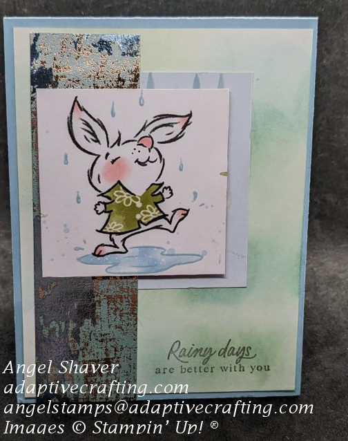 Blue card with background created with blue and green inks applied with a blending brush.  Card features a rabbit dancing in a puddle in the rain.  Sentiment says, "Rainy days are better with you."