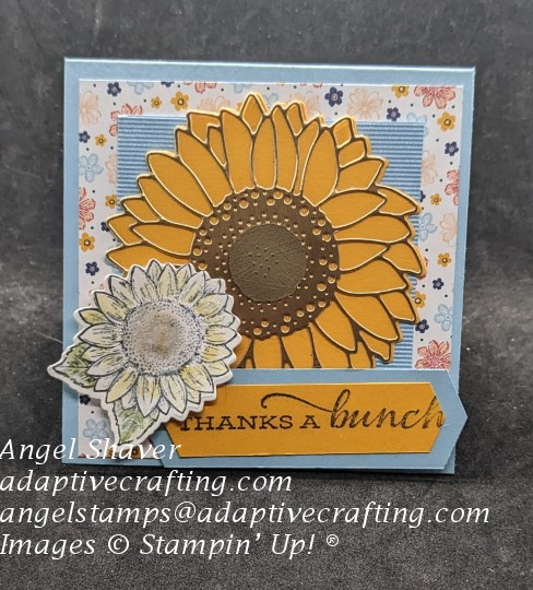 Blue thank you card with layers of floral patterned and textured paper.  Diecut sunflower and smaller one colored with blender pens.  Sentiment says "thanks a bunch."
