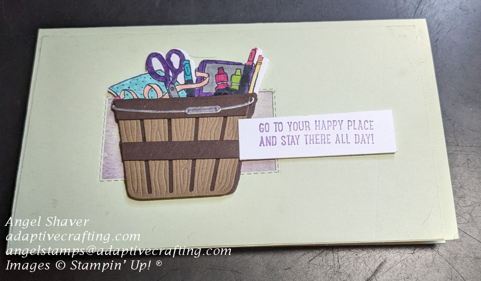 Light green slimline card with purple rectangle.   Die cut basket of craft supplies is over rectangle with sentiment that says "Go to your happy place and stay there all day!"
