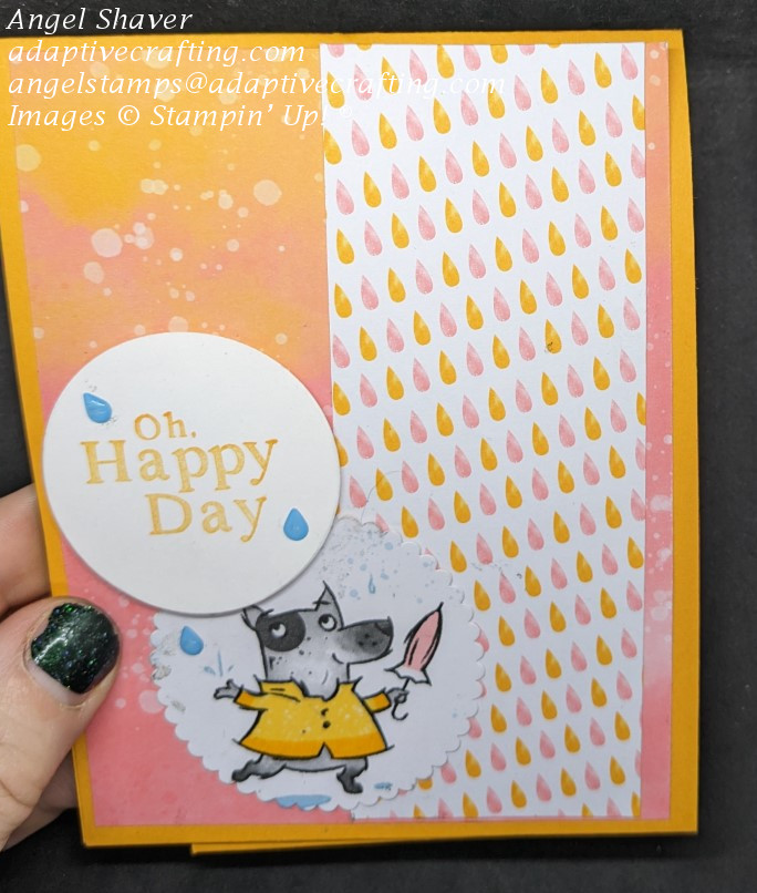 Orange card with  patterned paper with pink and orange raindrops.  Circle with dog with rain coat and umbrella and circle with sentiment that says, "Oh Happy Day" and raindrop embellishments.