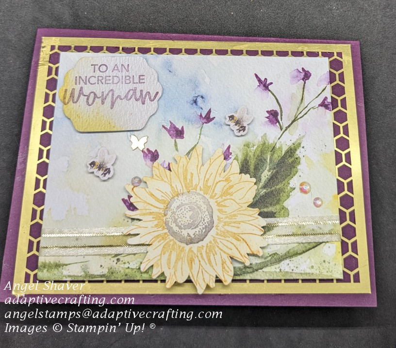 Purple mother's day card with layer of gold honeycomb paper.  Layer of watercolored look paper with flowers on top.  Bee dies, butterfly, stamped sunflower die, gold and vanilla ribbon, and iridescent rhinestones added to the card.  Sentiment label says "to an incredible woman."