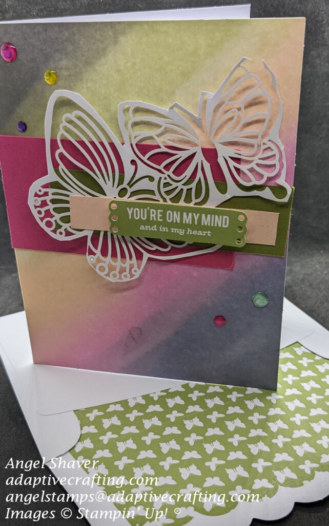 Card with rainbow wash background.  Strips of cardstock in bright pink, green, and lighter pink.  Cut out butterrflies are featured on the card front.  Sentiment says, "You're on my mind and in my heart."  Includes envelope with green lining with white butterflies