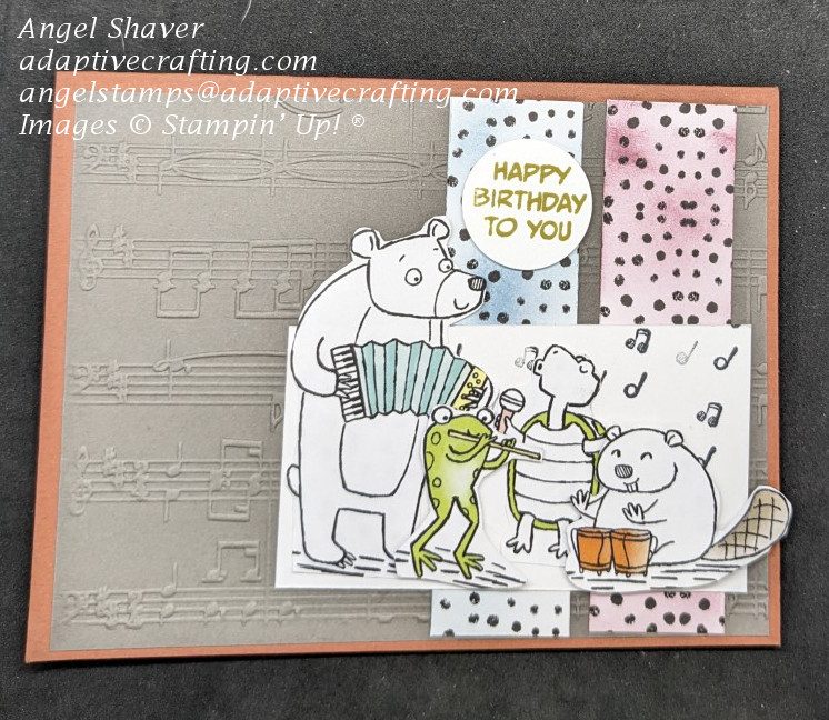 Copper Clay cardstock card with gray layer embossed with music.  Two strips of cardstock with black dots on right side colored with blending brushes--one blue and one mauve.  Band of fussy cut animals are performing on top layer.  Circle sentiment says "Happy Birthday to You."