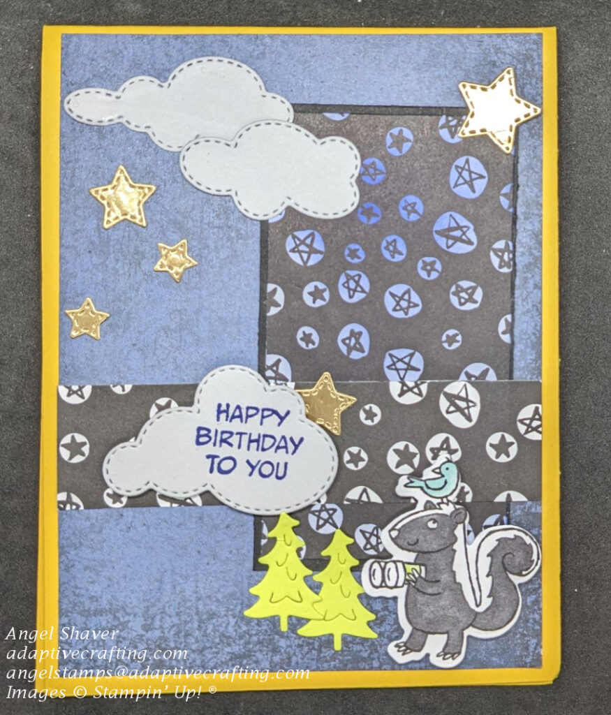 Yellow card with navy background paper representing the sky.  There are rectangle strips of patterned paper with stars and die cuts of grey clouds and gold stars.  One cloud says, "Happy Birthday to You."  The bottom of the card features a skunk die holding binoculars with a bird on his head.  There are also dies of green trees.