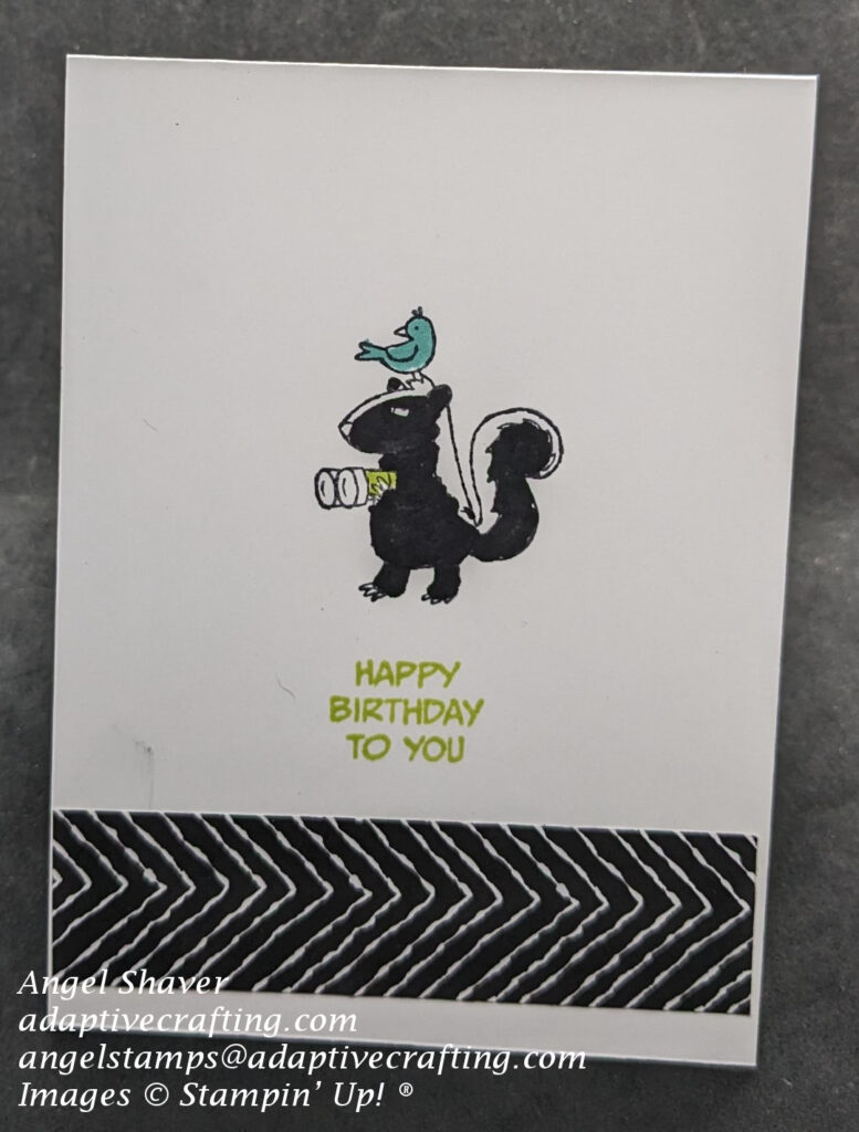 White birthday card with stamped skunk image holding binoculars with bird on his head at center of card.  Sentiment is stamped directly under skunk and says, "Happy Birthday to you."  Black and white patterned paper strip across bottom of card front.