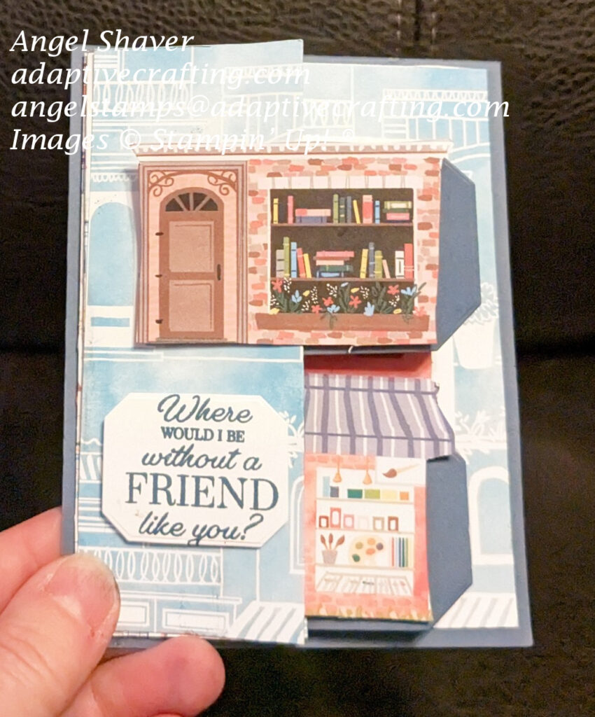 Fun fold 2,4,6,8 blue card featuring Les Shoppes blue patterned paper with white store outlines. The card highlights  a book store and an art store in full color on tabs of card.  Sentiment label on front says, "Where would I be without a friend like you?"