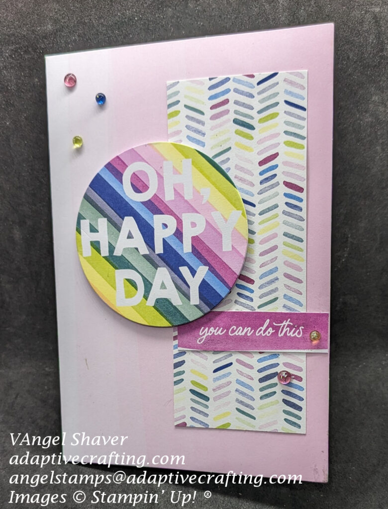 Pink ombre card with strip of patterned paper with colorful slated dashes.  Topped with sentiment  circle with multi-colored stripes that says, "One Happy Day" and a smaller rectangle label that says "you can do this."  There are also five tinsel dot embellishments.