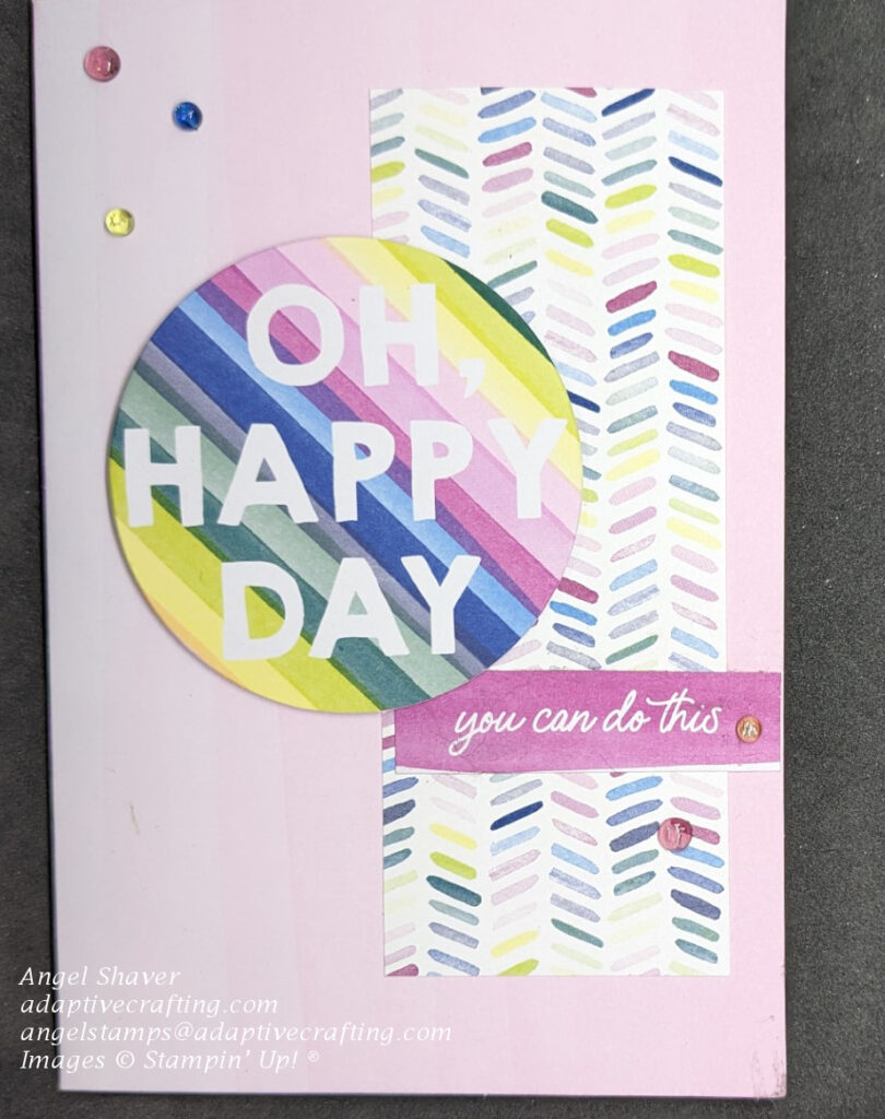 Pink ombre card with strip of patterned paper with colorful slated dashes.  Topped with sentiment  circle with multi-colored stripes that says, "One Happy Day" and a smaller rectangle label that says "you can do this."  There are also five tinsel dot embellishments.