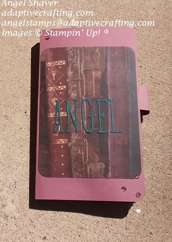 Mauve pencil case shown closed.  Front feature patterned paper with books and diecut letters that say "Angel".  Front is decorated with enamel and sparkle dots.