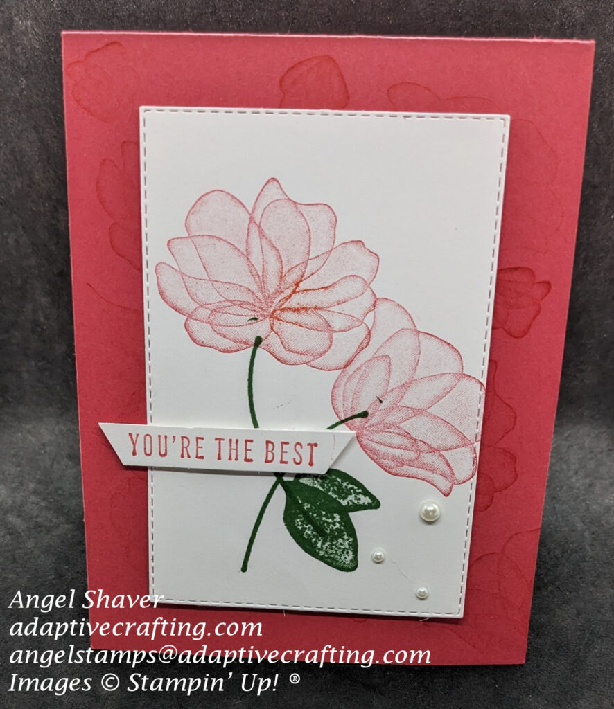 Red card with stamped tone on tone images of flowers creating background.  Stitched rectangle die creates top focal point with two stamped red flowers with green stalks and leaves.  Sentiment label says, "You're the Best."   Three pearls are added to white rectangle die.