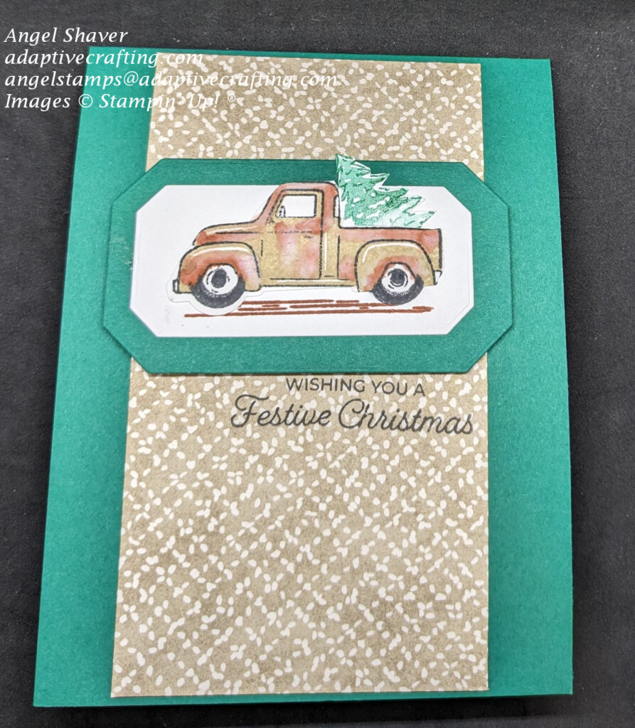 Green Christmas card with strip of light brown patterned paper rectangle with white cross hatching down center of card front.  Tan vintage truck stamp with rust blooms all over the truck is the featured image and is framed with a green hexagon frame.  Truck bed is carrying a Christmas tree. Stamped sentiment says, "Wishing You a Festive Christmas."