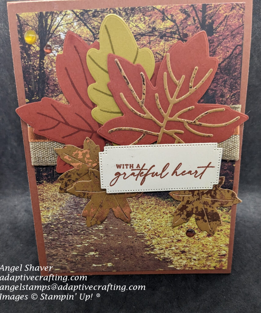 Brown fall card with colored fall leaves patterned paper, stamps, and dies.  Both natural and copper ribbon surround the center of the card front to add a base for the diecut leaves.  Sentiment label says "with a grateful heart."