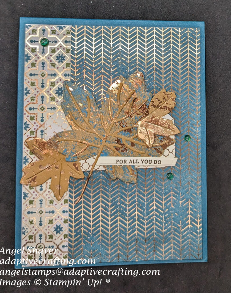 Teal card with two patterned papers featuring teal and copper that create background layer.  Diecut maple leaves are center focal point on cream and copper hexagon die.  Sentiment label says, "For all you do".  Card front decorated with three teal tinsel dots.