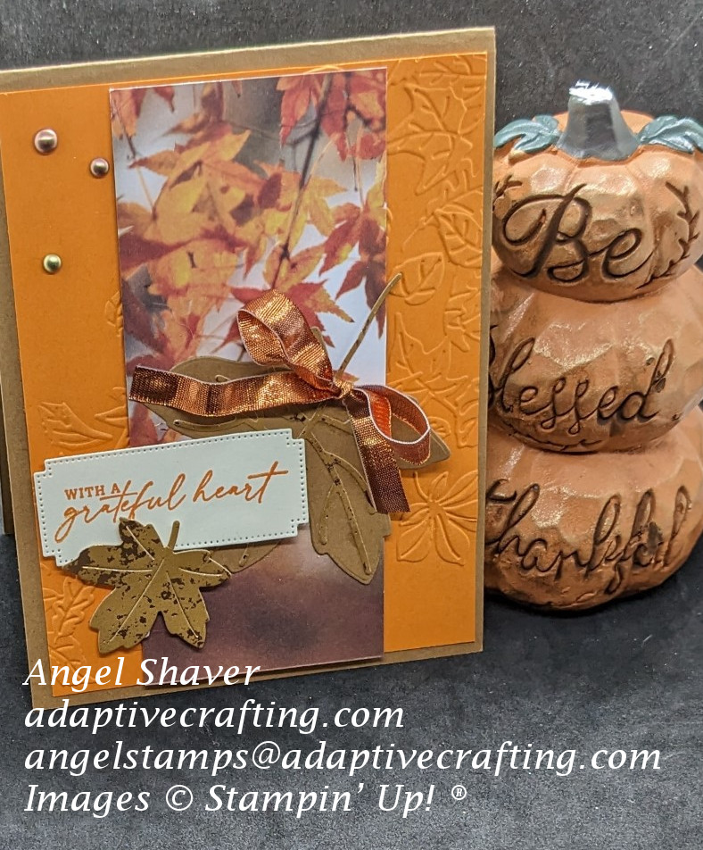 Brown thanksgiving card with orange card layer embossed with falling leaves.  Strip of patterned paper featuring leaves on top of that with maple leaf dies.  Sentiment label says, "with a grateful heart."  Large leaf is tied with a copper ribbon.  Metallic dots add bling.