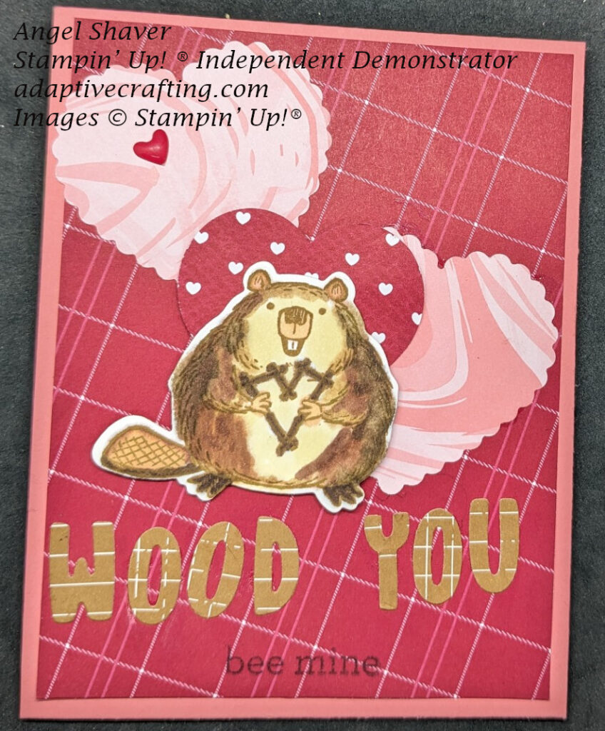 Pink card with red and pink plaid card layer.  Three punched hearts are in the center: 2 scalloped pink marble print and one red with small white hearts.  Beaver die holding a heart made with sticks is the focal image.  The bottom has brown and white die letters that say, "wood you" and bee mine is stamped underneath.