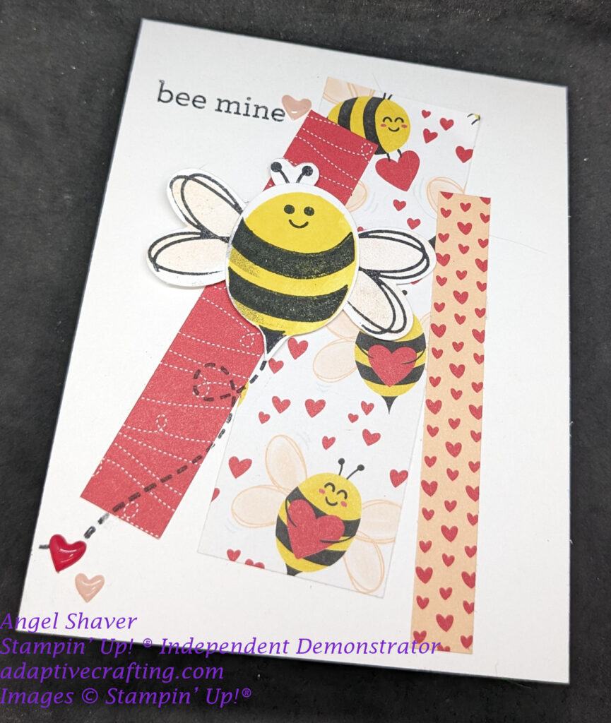White Valentine with strips of red and pink patterned paper featuring hearts and bees.  Focal point bee punch in center of card with stamped flight pattern line.  Sentiment says, "Bee Mine."  Card finished with red and pink enamel hearts.