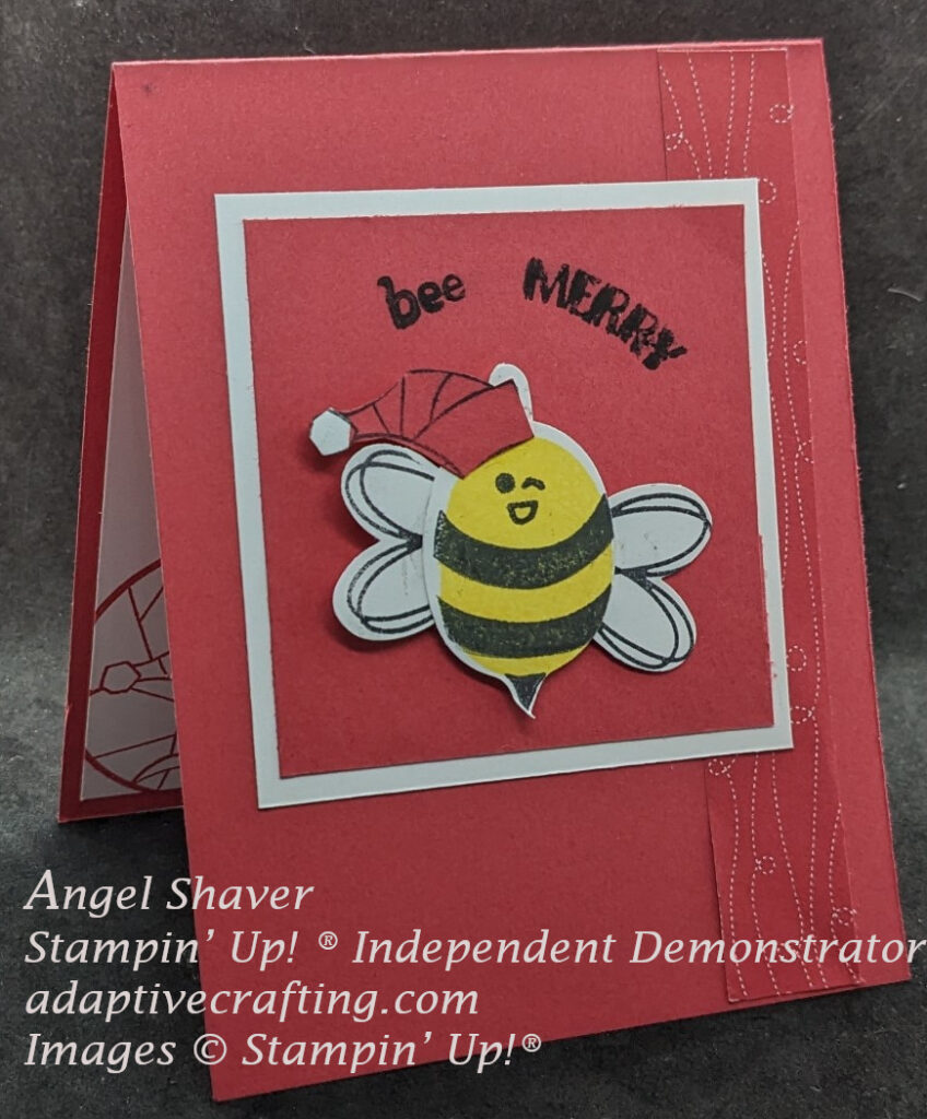 Red Christmas card with strip of patterned paper with flight lines on the right side of card front.  Focal point of card is a red square framed by a white square square containing a bee die wearing a Santa hat.  Sentiment says, "Bee Merry."