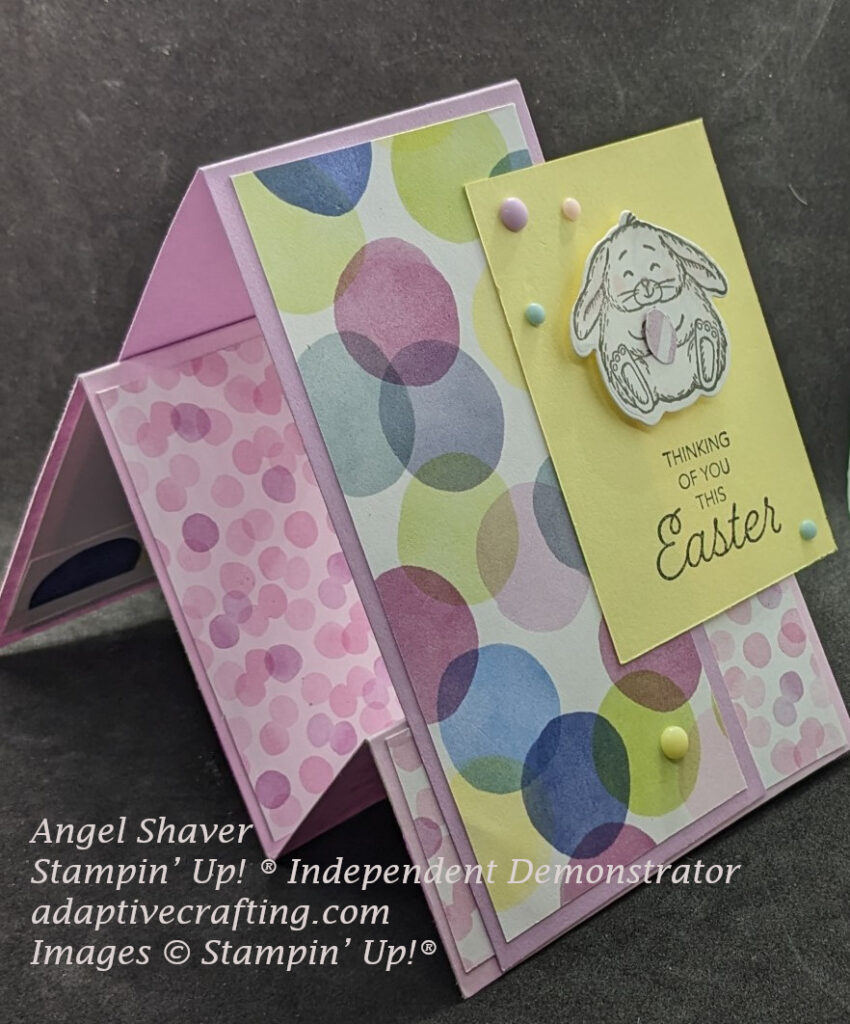 Angle view of pink faux step card with purple tent.  Card has polka dot patterned paper.  Yellow rectangle featuring a die cut bunny holding an Easter egg.  Sentiment says "Thinking of ou thie Easter."