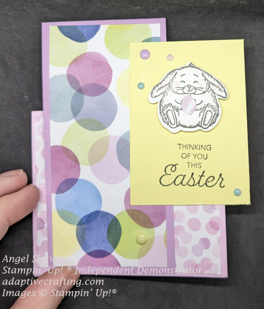 Front view of pink faux step card with purple tent.  Card has polka dot patterned paper.  Yellow rectangle featuring a die cut bunny holding an Easter egg.  Sentiment says "Thinking of ou thie Easter."