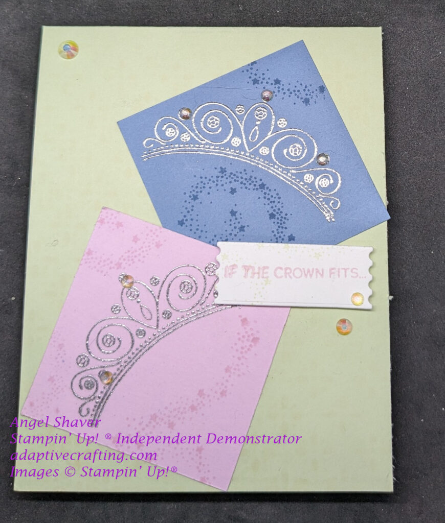 Green card with pink and blue squares on the card front.  Each square has a silver heat embossed crown along with tone on tone swirling stars.  There is a white sentiment label with pink "If the crown fits . . ."  Iridescent Rhinestones are decorating crowns and adding bling to the card front.