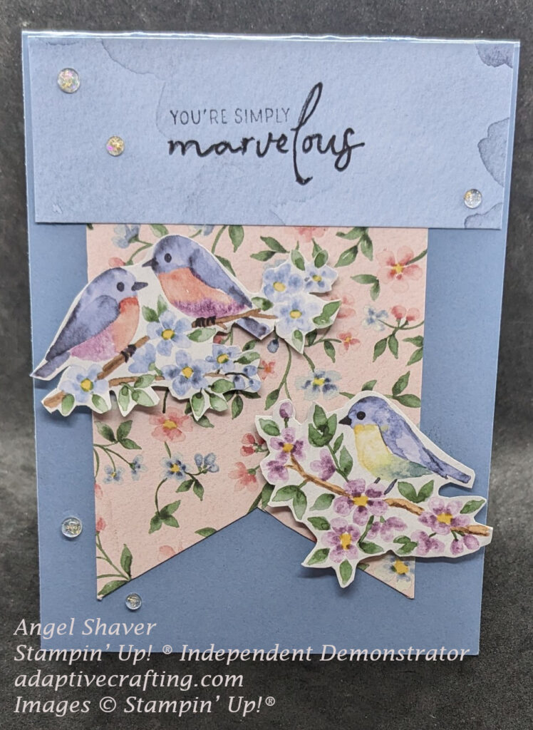 Blue card with pink tag covered in pink and blue flowers on large flag shape hanging from top sentiment banner.  Images of birds on flowered branches are on either side of flag.  Sentiment says, "you're simply marvelous."