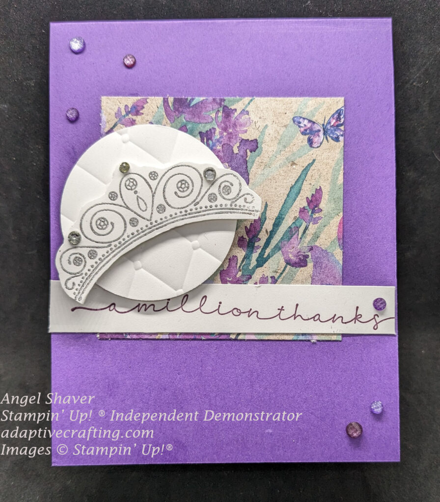 Purple card with square of patterned paper featuring lavender and a butterfly.  Tufted embossed circle with silver crown with rhinestones on top.  Sentiment says, "A million thanks"  Card finished with purple gems.