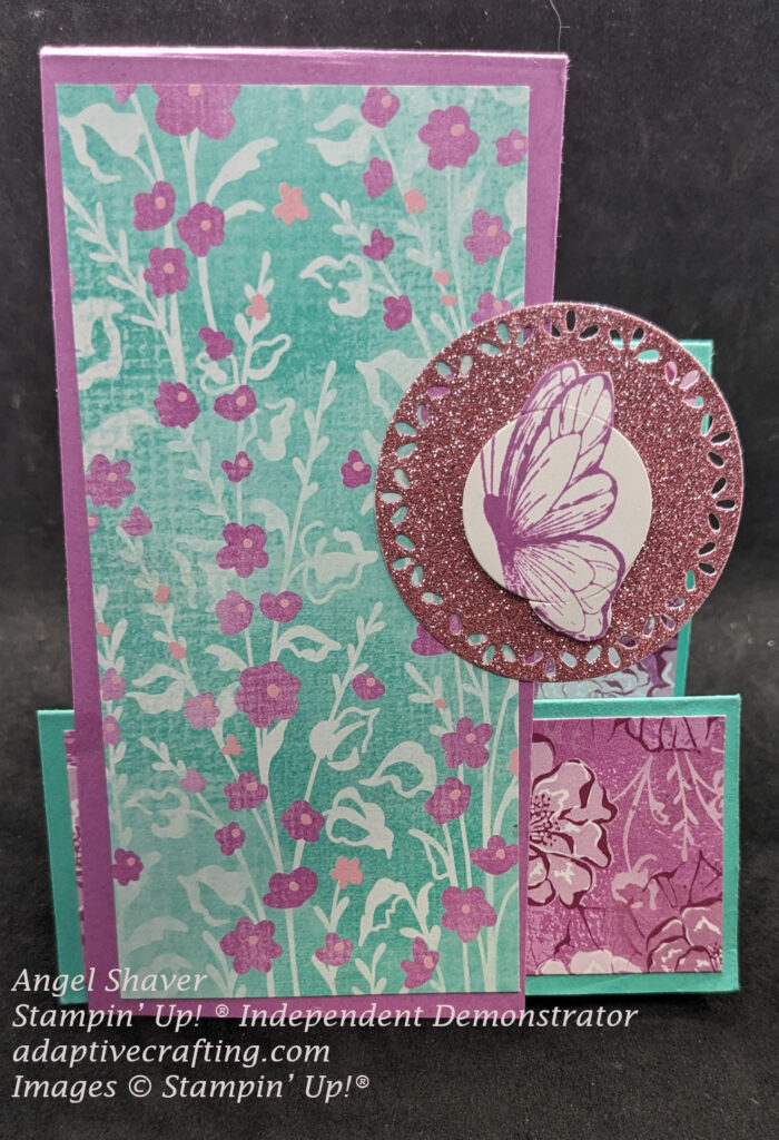 Teal and purple faux step card with foloral patterned paper in purple and teal with some pink flowers..  Circle cut from pink glimmer paper is the focal point with a purple butterfly on it.