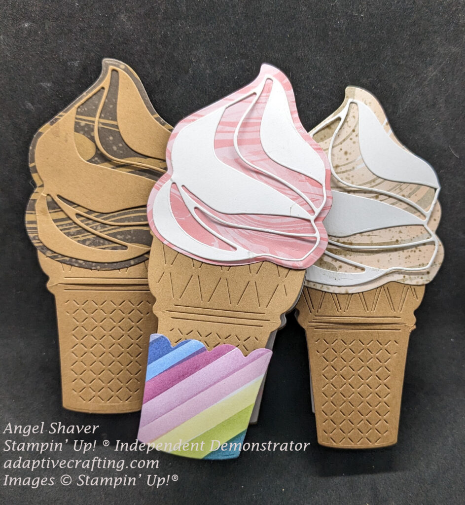 Three shaped swirl ice cream cone cards.  One has dark brown and lighter brown swirled patterned paper with a lighter brown cardstock swirl.  One had a pink and darker pink swirled patterned paper with a white cardstock swirl.  It has a bright diagonal striped paper cone holder.  One has light pink and light brown swirled patterned paper with a white cardstock swirl.