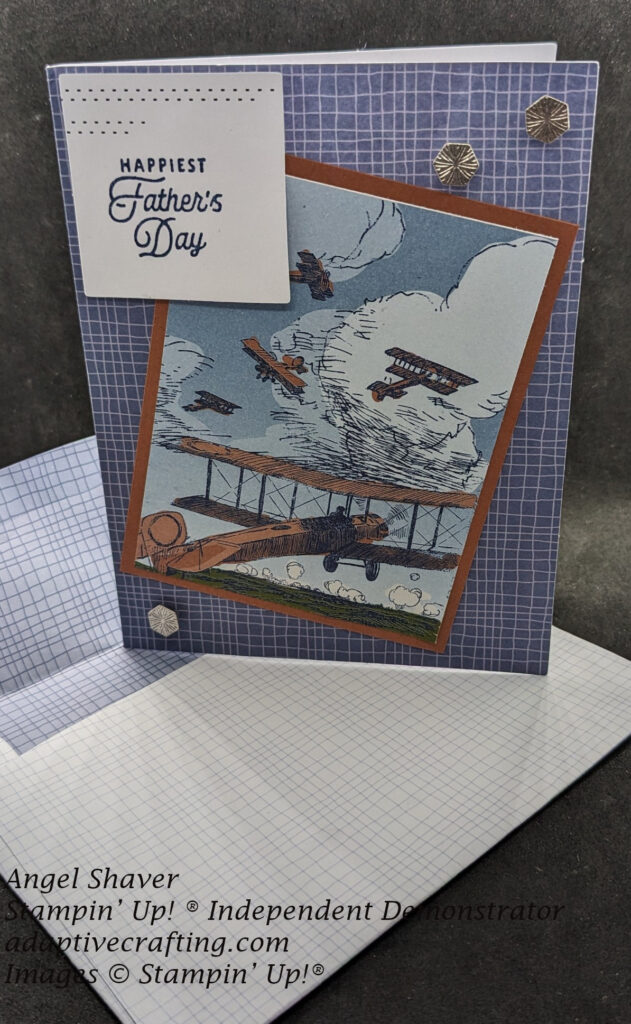 Blue and white checkered pre-printed card.  Front of card has pre-printed panel of vintage airplanes flying through a cloudy sky.  Printed panel is framed by  copper clay colored cardstock.  White label with blue dots across top is stamped with "Happiest Father's Day".  Three silver hexagon trinkets are added.