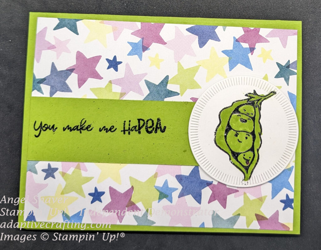 Green card with patterned paper layer of bright, multicolored stars.  There is a green strip of paper across middle of card with sentiment "You make me HaPEA" heat embossed in black.  White circle die with slash marks embossed around outside of circle is on the right edge of the sentiment strip.  Circle is stamped with a pea pod showing four peas with cartoon faces.  Pea pod is heat embossed with black embossing powder and colored with green marker.