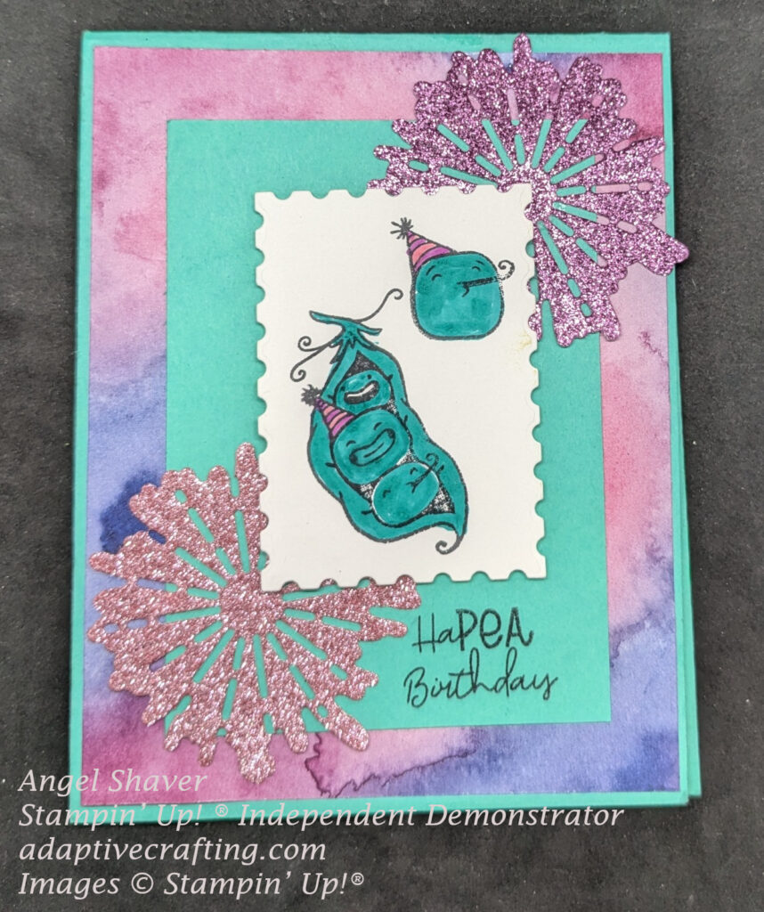 Turquoise green birthday card with layer of patterned paper with pink and purple splotches.  Turquoise green rectangle on top of that with white rectangle with postage stamp edges on top.  Pod of three celebrating peas along with an individual pea wearing a party hat with a noise blower are stamped on the postage rectangle die and colored in.  A pink and purple glimmer firework die and adhered under to right and bottom left corners of the postage die.  The sentiment "HaPEA birthday" is stamped at the bottom of the turquoise rectangle.