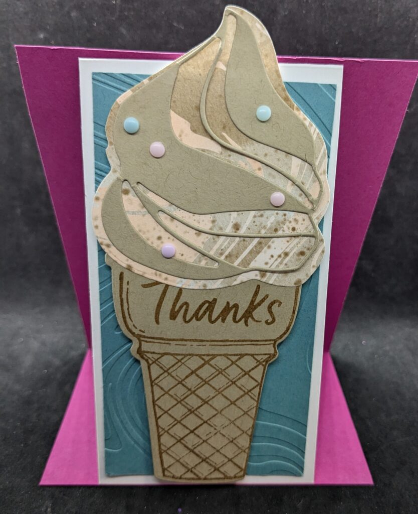 Pink cardstock panel with thinner white thank you card attached to pink panel.  Pink panel is open with thinner white thank you card standing upright tent style.  Outside of thinner white card has panel of clue cardstock embossed with swirl pattern.  On top of that is a diecut ice cream cone with pink and brown and white ice cream scoop with light brown swirled die cut on top.  Pastel adhesive dots are added on top of the ice cream to represent sprinkles.  The cone says, "Thanks."