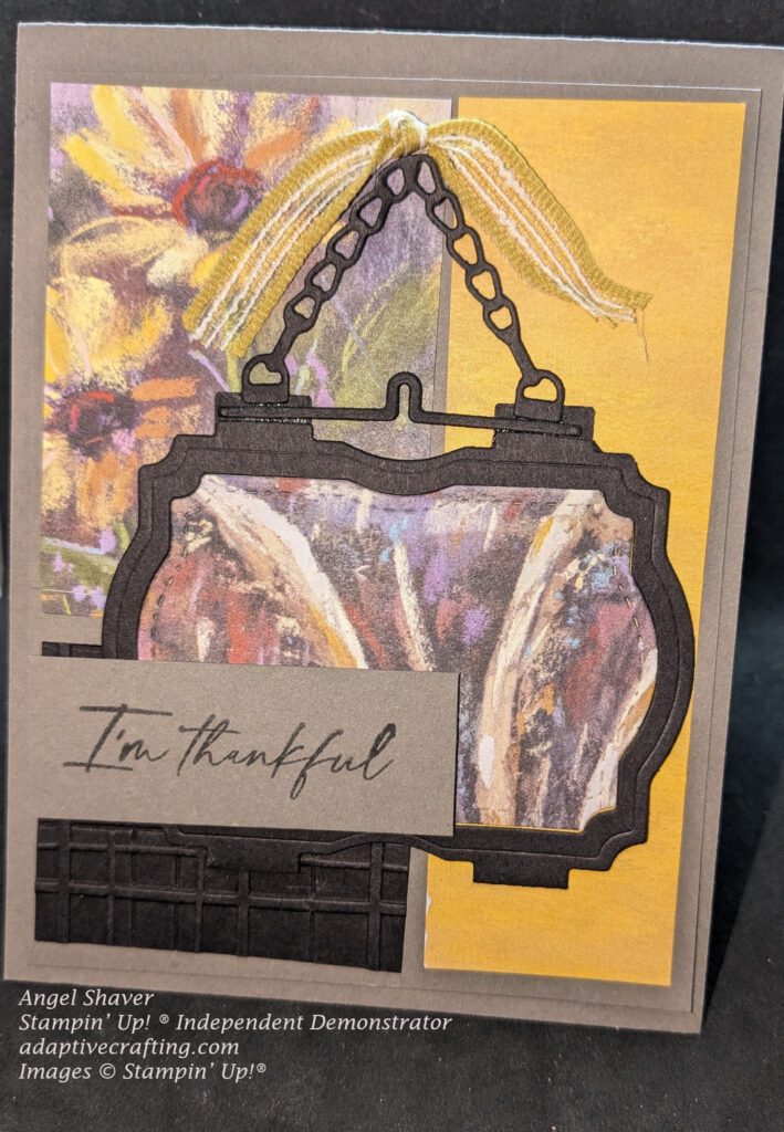 Grey thank you card featuring panels of yellow, black, and sunflowers on the card front.  Black panel is embossed with plaid.  Featured black frame die with hanging chain frames patterned paper featuring shocks of wheat.  The frame is hanging from a yellow knotted ribbon.  The gray sentiment label says, "I'm thankful."  