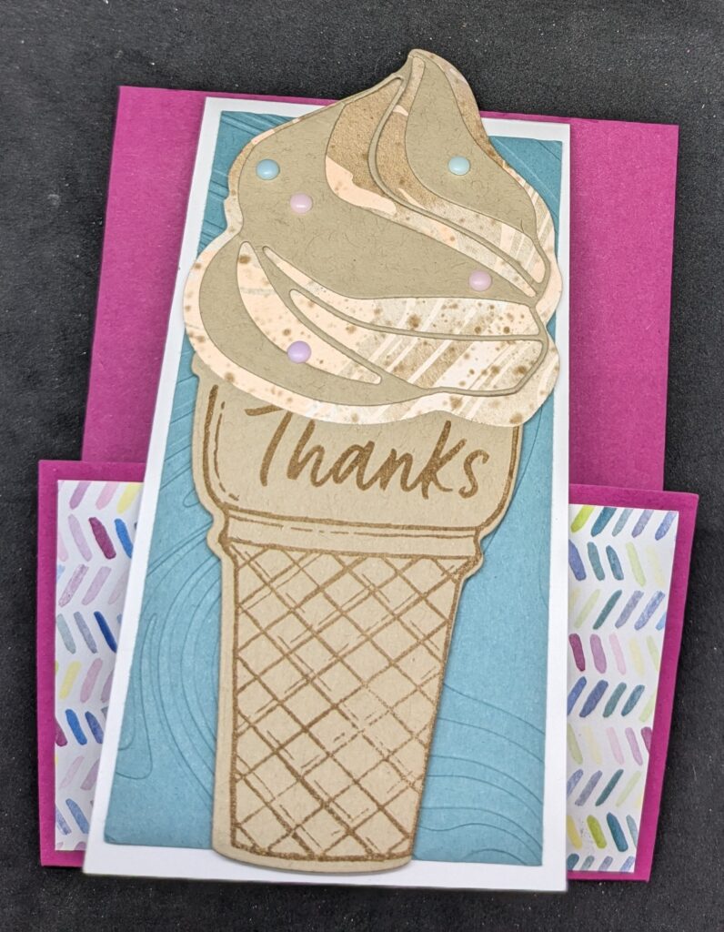 Pink cardstock panel with thinner white thank you card attached to pink panel.  Bottom part of pink cardstock is folded up inside of white thank you card and has patterned paper with bright small diagonal slash marks in various bright colors on it.  Outside of thinner white card has panel of clue cardstock embossed with swirl pattern.  On top of that is a diecut ice cream cone with pink and brown and white ice cream scoop with light brown swirled die cut on top.  Pastel adhesive dots are added on top of the ice cream to represent sprinkles.  The cone says, "Thanks."