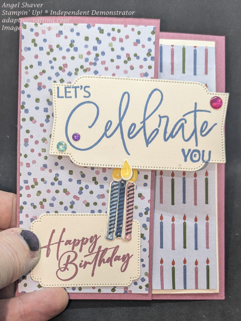 Pink birthday card with patterned paper of blue, green, and pink confetti on card front..  A sentiment label says, "Let's Celebrate You" and is only adhered to front of card by left half of card.  Bottom of card front has a label that says, "Happy Birthday" and has three candle dies.  The inside of card has strip of patterned paper with candles that you can see when card is closed.