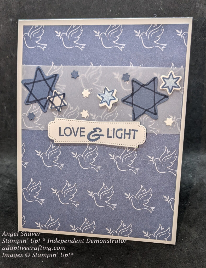 White Hanukkah card made with layer of blue patterned paper with doves on it.  Strip of vellum is on top part of card and Star of David shaped dies are layered on it in blue and white and three different sizes.  Sentiment label is at bottom of vellum strip and says, "Love & Light"