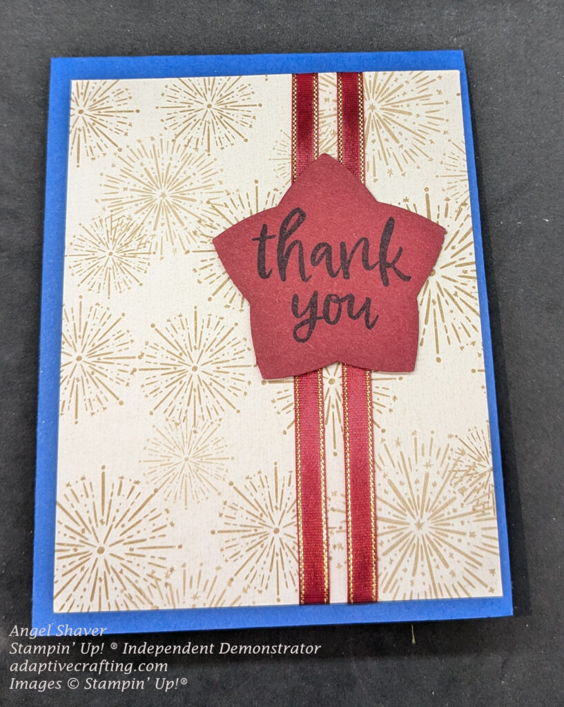 Blue thank you card with fireworks patterned paper as the background layer.  There are two stripes of red ribbon trimmed in gold.  There is a star punch on top of the ribbons that says, "thank you."