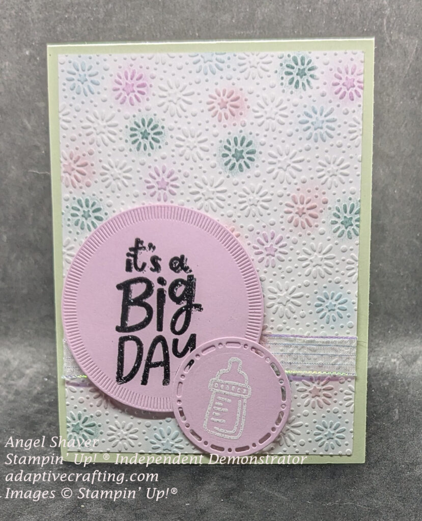 Green card with embossed starbursts colored with pink, purple, blue, & green.  Iridescent ribbon across bottom of card and two pink circles.  The larger one heat embossed in black, "It's a big day." Smaller pink circle with bottle heat embossed in white.